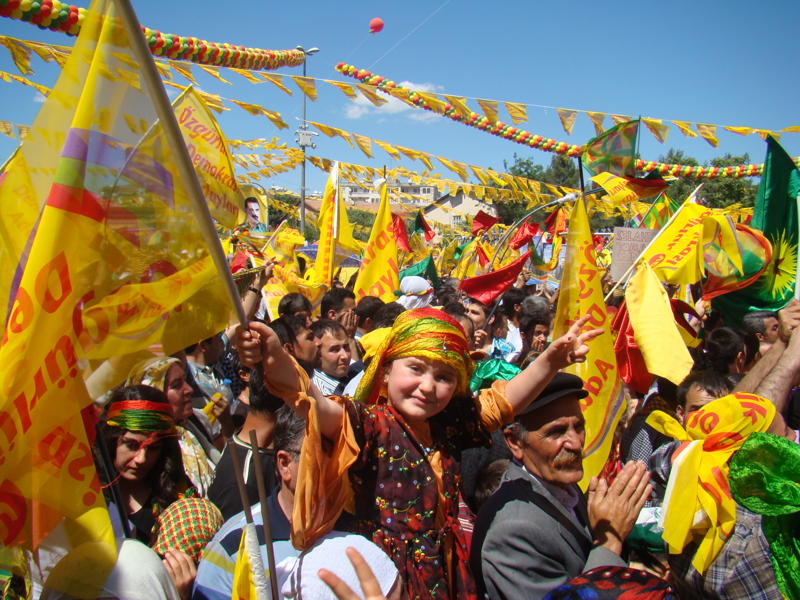 Image of Kurdish people dressed brightly in a rally with a blue sky